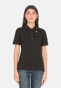 Polo nero con colletto, caratterizzato da una chiusura a cinque bottoni e un piccolo logo sul petto sinistro. Maniche corte e materiale in cotone.