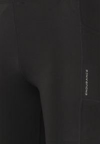 Zwarte atletische leggings gemaakt van gladde, rekbare stof. Bevat een zijvak en zichtbare stiksels met het 'ENDURANCE' logo in zilver.