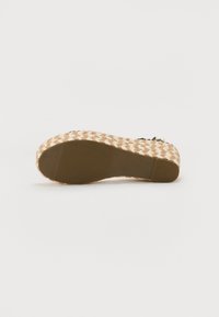 Sandal en plateforme tissée beige avec une semelle texturée en jute et un pied en caoutchouc lisse. Comprend une sangle décorative avec des accents noirs.