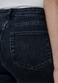 Jean en denim bleu marine présentant un gros plan de la poche arrière et de la taille. Le tissu a une texture lisse avec des détails de décoloration subtils.