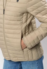 Bēšas krāsas pūkaina jaka ar horizontālu šķautnēto dizainu, priekšā rāvējslēdzēju un sānu kabatām. Mīksta faktūra un elastīgas aproces.