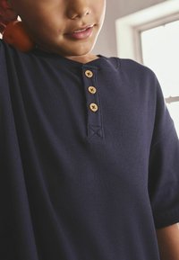 Dunkelblaues, geripptes T-Shirt mit Rundhalsausschnitt und vier Holzknöpfen. Der Stoff hat eine strukturierte Oberfläche und einen lockeren Schnitt.