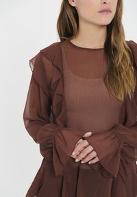Maroon, sheer dress with frilled sleeves and hem. Textured fabric with a slightly sheer quality. Features a fitted bodice and flowing shape.