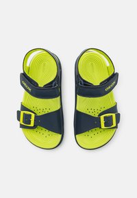 Sandalias azules y verde lima con un diseño moldeado, que cuentan con una correa de hebilla y agujeros de ventilación para mejorar la transpirabilidad. Marca Geox en la correa.