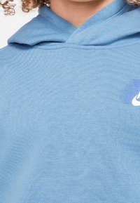 Light blue hoodie featuring a textured fabric, adjustable drawstring hood, and a white logo on the front. Simple and functional design.