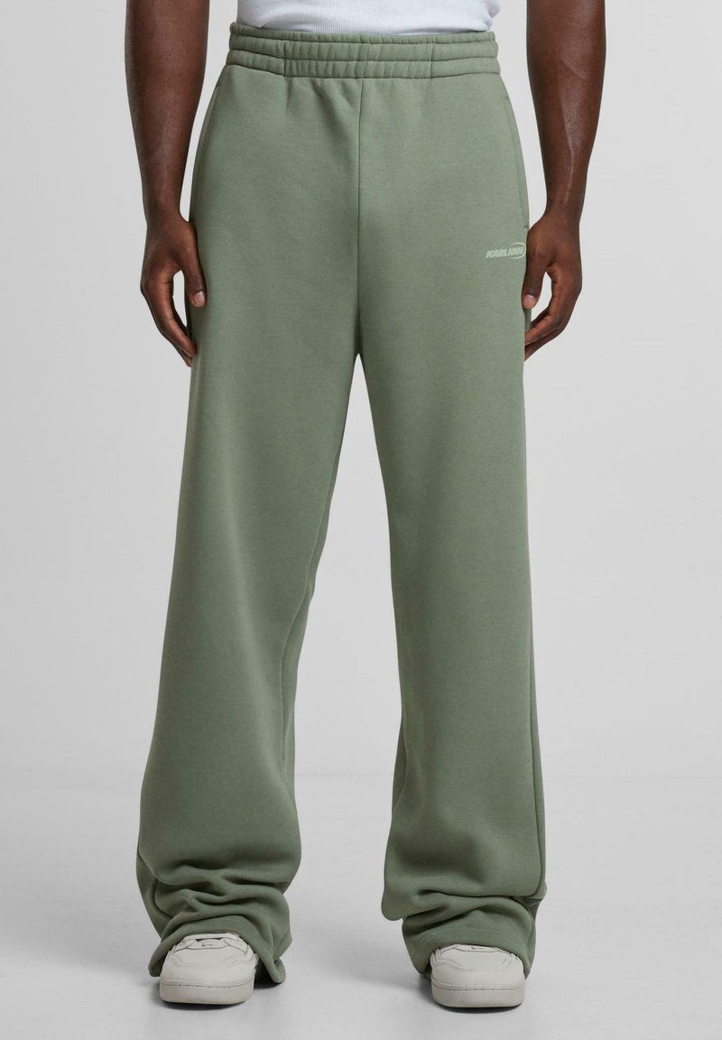 Light green sweatpants with a relaxed fit, elastic waistband, side pockets, and a smooth texture. Features subtle branding on the thigh.