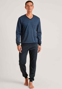 Marineblauw langemouwen V-hals top met lichtblauwe stippen, gecombineerd met donkere broek met elastische boorden voor een comfortabele pasvorm.