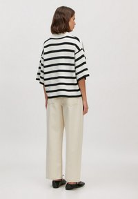 Gestreepte gebreide trui in zwart en wit, korte mouwen, relaxed fit. Gecombineerd met crèmekleurige wijde broek en zwarte platte schoenen.