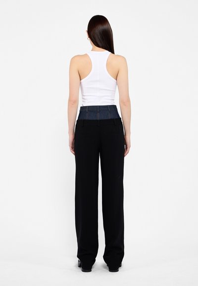 White sleeveless tank top paired with black wide-leg trousers featuring a denim waistband. Smooth texture, minimal design, and tailored fit.