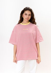Rood-wit gestreepte oversized t-shirt met een gele kraag en een klein logo op de borst. Katoenen materiaal, korte mouwen, losse pasvorm.