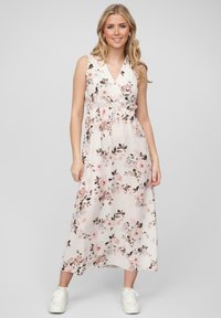 Florale maxi-jurk van lichtroze stof met een V-hals, elastische taille en witte sneakers. Heeft een patroon van roze bloemen en groene bladeren.