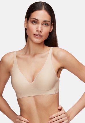 Bra wireless beige con design a scollo a V, spalline regolabili e una texture liscia e senza cuciture. Tessuto leggero per comfort e flessibilità.