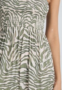 Green and beige dress with a smocked bodice and flowing pleated skirt. Features a wavy zebra-like pattern in contrasting colors and smooth texture.