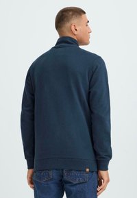 Tumši zilas krāsas krekls ar augsto apkakli un garām piedurknēm. Iespējas ribotu piedurkņu un apakšmalu, izgatavots no mīksta kokvilnas maisījuma auduma.