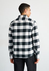 Camisa a cuadros en blanco y negro, con cuello recto, mangas largas y un corte relajado; presenta un patrón de cuadros en contraste y puños.