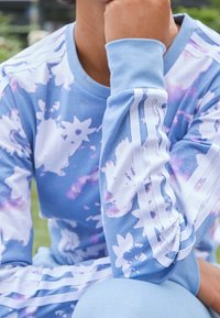 Blå långärmad skjorta med blommönster och vita ränder på ärmarna. Mjuk tyg och avslappnad passform. Har en rund halsringning.