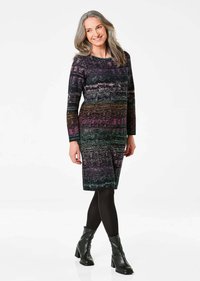 Robe en tricot à manches longues, avec un motif multicolore dans des nuances de noir, violet et vert. Longueur genou, associée à des collants noirs et des bottes à la cheville.