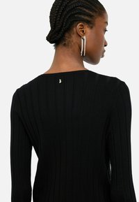 Top in maglia a coste nera con scollatura tonda e un dettaglio dorato sul retro, maniche lunghe e silhouette aderente.