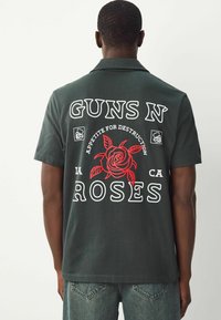 Černé tričko s krátkým rukávem, které zdobí velká grafika červené růže a text "GUNS N' ROSES" s "APPETITE FOR DESTRUCTION" ve bílé barvě. Pohodlný střih.