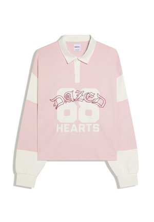 Langærmet pink og hvid rugbyshirt med hvid krave, knaplukning, teksten "DAZED 86 HEARTS" på forsiden og hvide ærmekanter.