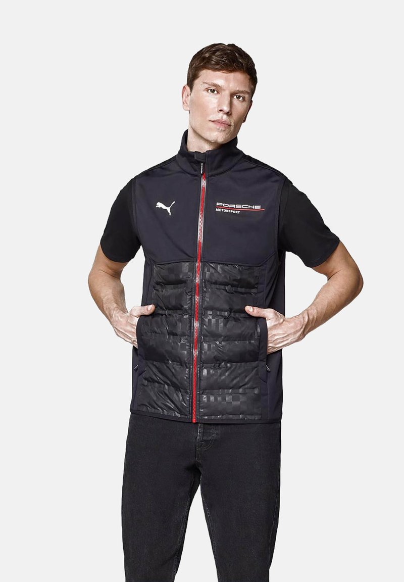 Czarna kamizelka z ocieplaną przodem, czerwonym zamkiem błyskawicznym i logo Porsche Motorsport. Wykonana z lekkiego materiału, o eleganckim kroju i dwóch kieszeniach.