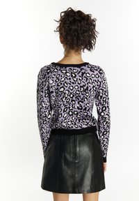Pulover cu imprimeu de leopard mov, cu guler și manșete negre în vrac, asortat cu o fustă mini din piele neagră, văzut din spate.