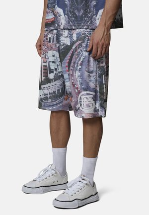 Męski model noszący białe sneakersy, białe skarpetki z mankietem oraz szorty z nadrukiem widoku miasta z lotu ptaka, pokazany od połowy uda w dół.