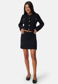 Svart tweed co-ord-set som består av en kort jacka med guldknappar och två framfickor, ihop med en figurnära mini kjol.