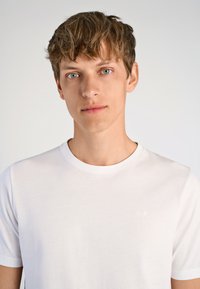 Biała koszulka z krótkim rękawem, wykonana z miękkiego materiału, z okrągłym dekoltem i subtelnym logo góry na lewej piersi.