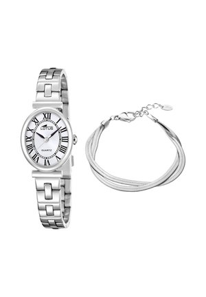 Srebrny zegarek na nadgarstek z białą owalną tarczą i rzymskimi cyframi obok srebrnej bransoletki z wieloma łańcuszkami, zapinanej na zapięcie typu karabińczyk.