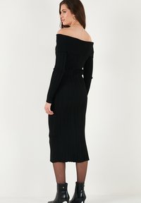 Musthave mustribu seeliku bänneritega, pikkade varrukatega, figuuri rõhutav siluett, põlvekohale ulatuv ääreline ja mustad pahkluudega saapad.