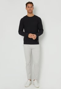 Pull en maille noir texturé avec un col rond, associé à un pantalon slim beige clair et des baskets blanches. Design simple avec des accents minimaux.