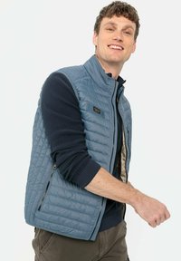 Hellblauer, gesteppter Puffer-Westen mit Reißverschlusstaschen, kombiniert mit einem dunkelblauen, gerippten Langarmshirt. Glatte Stofftextur, lässige Passform.