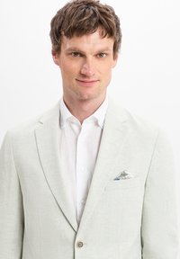 Hellgrauer Leinenblazer mit zwei Knöpfen, Reverskragen und einem Einstecktuch mit blau-weißer Musterung über einem weißen Hemd.