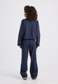 Ensemble de pyjama rayé marine comprenant une veste courte et un pantalon ample. Le matériau est doux avec des rayures claires contrastantes et des ourlets retroussés.
