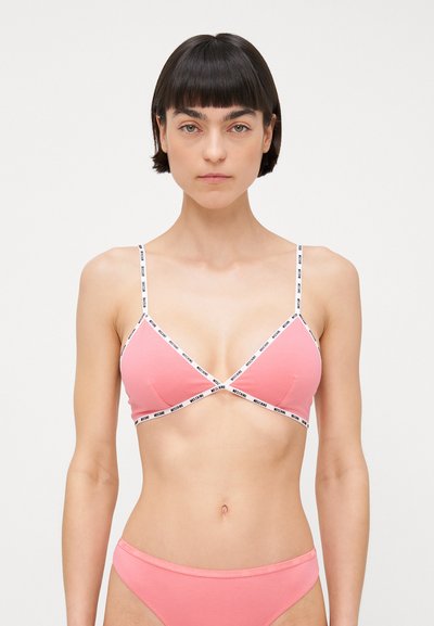 Růžový bavlněný bralet s bílými nastavitelnými ramínky. Obsahuje černé logo podrobnosti podél ramínek a má trojúhelníkový tvar. Hladká textura.