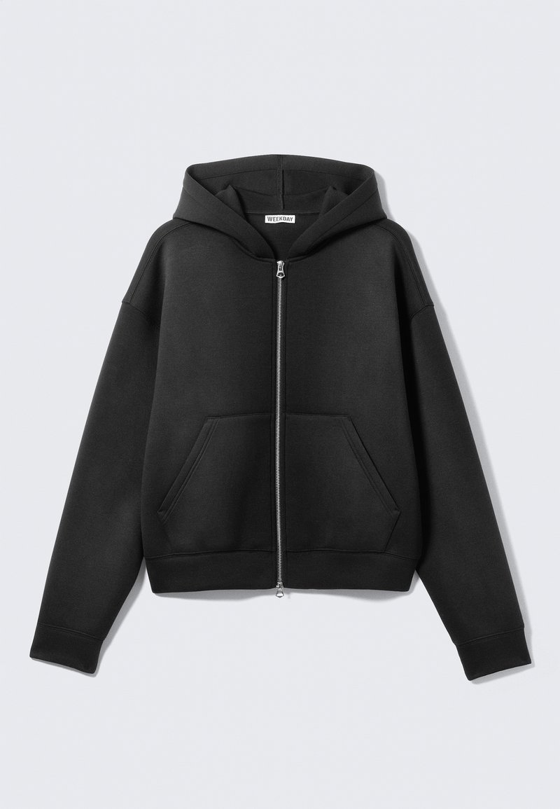 Sweat à capuche noir zippé en tissu doux, avec une poche avant, une capuche et des poignets côtelés. Design minimaliste sans motifs visibles.