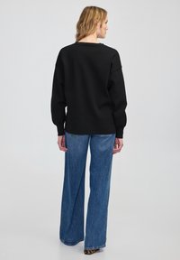 Zwarte trui met een ontspannen pasvorm, geribbelde textuur en een ronde halslijn, gecombineerd met blauwe denim broeken met brede pijpen.