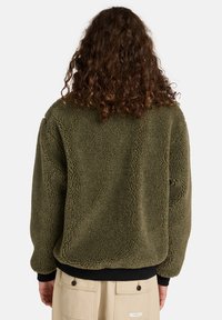 Veste en polaire olive avec une surface texturée. Dotée d'une taille et de poignets côtelés noirs, elle offre un design décontracté et confortable.