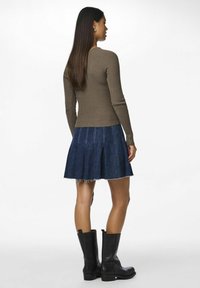 Prążkowana, brązowa bluzka z długim rękawem zestawiona z rozszerzaną, ciemnoniebieską spódnicą dżinsową z postrzępionym dołem i białym przeszyciem, uzupełniona czarnymi botkami za kostkę.