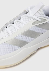 Hvid atletisk sko med mesh-overdel, sølvstribe detaljer, solid hvid sål og snørebåndsdesign med hæltab.