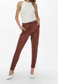 Brązowe zwężane spodnie z elastycznym pasem i sznurkiem, w połączeniu z białym halterem w prążki i białymi szpilkami.