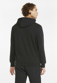 Fekete kapucnis pulóver, puha textúrával, laza szabással és bordázott mandzsettákkal rendelkezik. A hátoldal dizájnja egyszerű, figyelemre méltó minták nélkül.