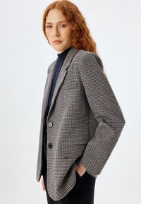 Grau, schwarz und burgunderfarbener Blazer im Hahnentrittmuster. Mit zwei Knöpfen, Reverskragen und einer lockeren Passform. Robuste Stofftextur.