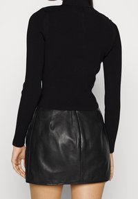Zwarte geribbelde top met lange mouwen, gecombineerd met een zwarte leren minirok met een gladde textuur en een aansluitend ontwerp.