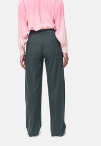 Wijd uitgesneden broek in donkergroen met witte streepjes, gepaard met een roze, gradient zijden blouse. De stof heeft een gladde textuur.