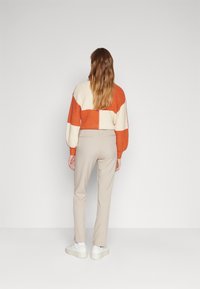 Pull en tricot oversize aux rayures orange et crème, associé à un pantalon beige ajusté et des baskets blanches à plateforme.