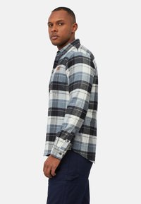 Geruit flanellen overhemd in blauw, grijs en zwart. Lange mouwen met knoopmanchetten, zijsplitten en een borstzak met een logo-patch.