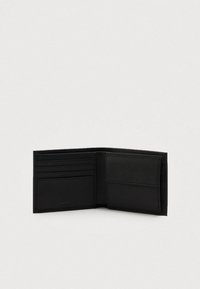 Čierna bifold peňaženka otvorená, s štyrmi slotmi na karty na ľavej strane a vreckom na mince s chlopňou na pravej strane, s embosovaným logom značky.