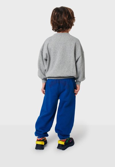 Felpa grigia con vestibilità oversize e polsini a costine, abbinata a pantaloni da jogging blu vivaci con vita elastica e dettaglio logo.